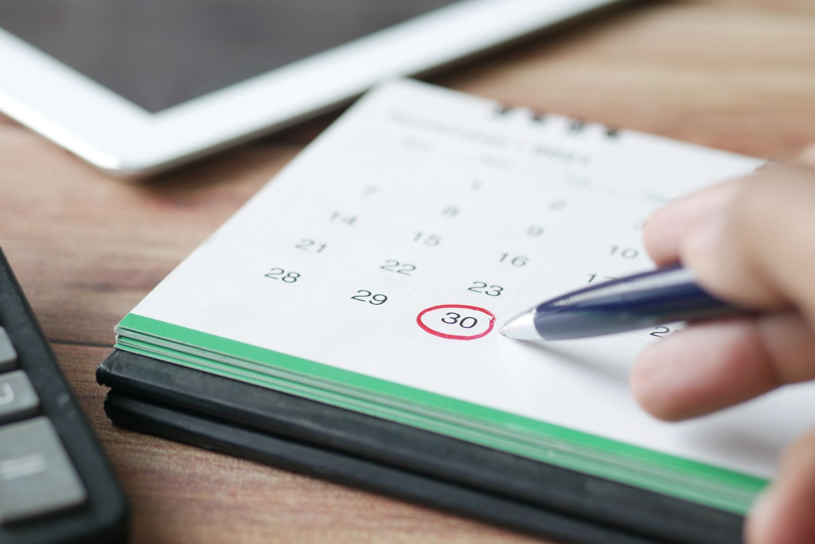 A hand holding a black pen over a paper calendar