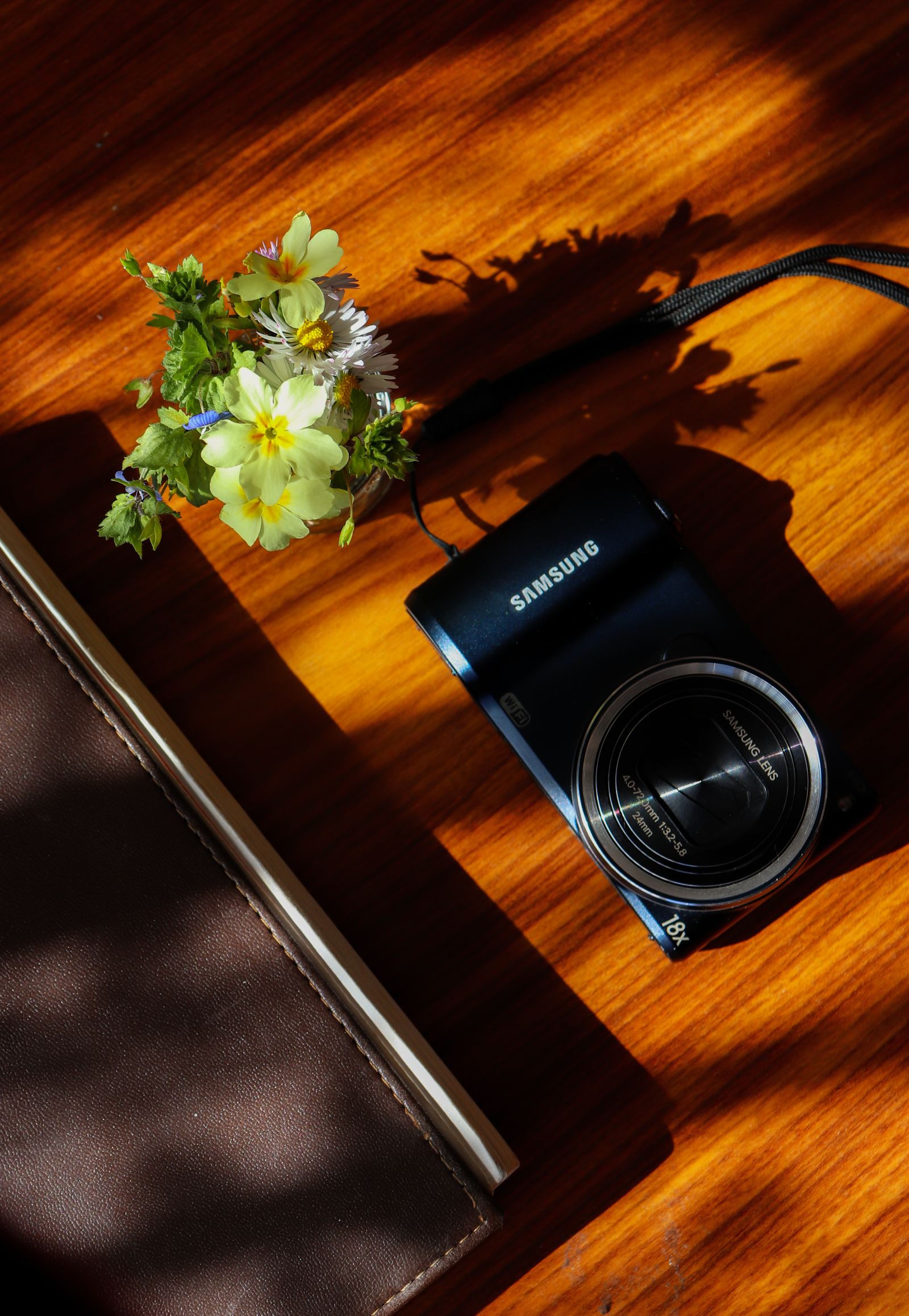 Compact digital camera, notebook and flowers on a wooden surface