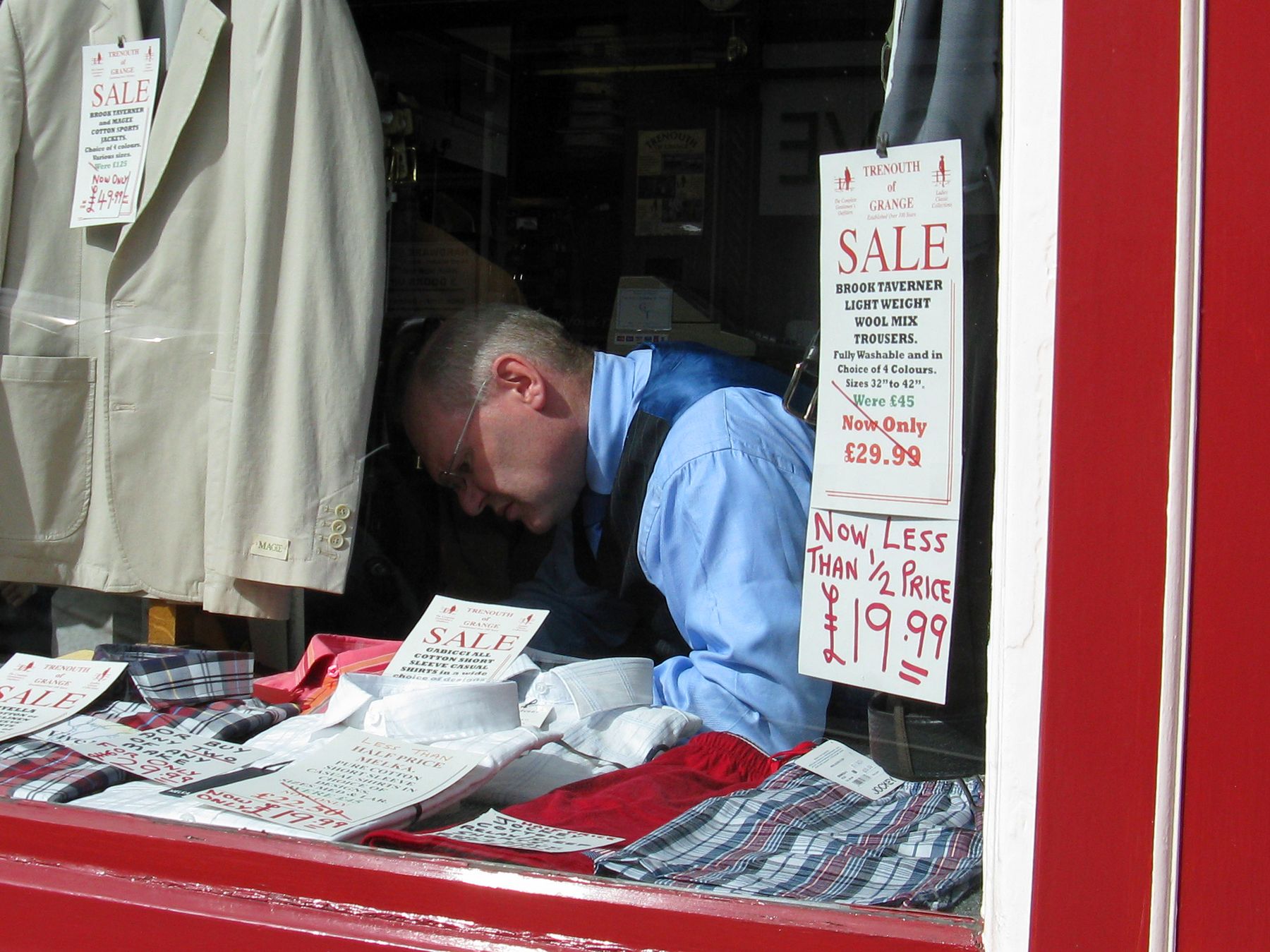 Shopkeeper arranging clothing in a window with sale signs